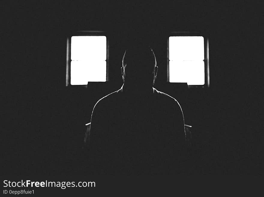 Person Sitting in Dark Room With 2 Window