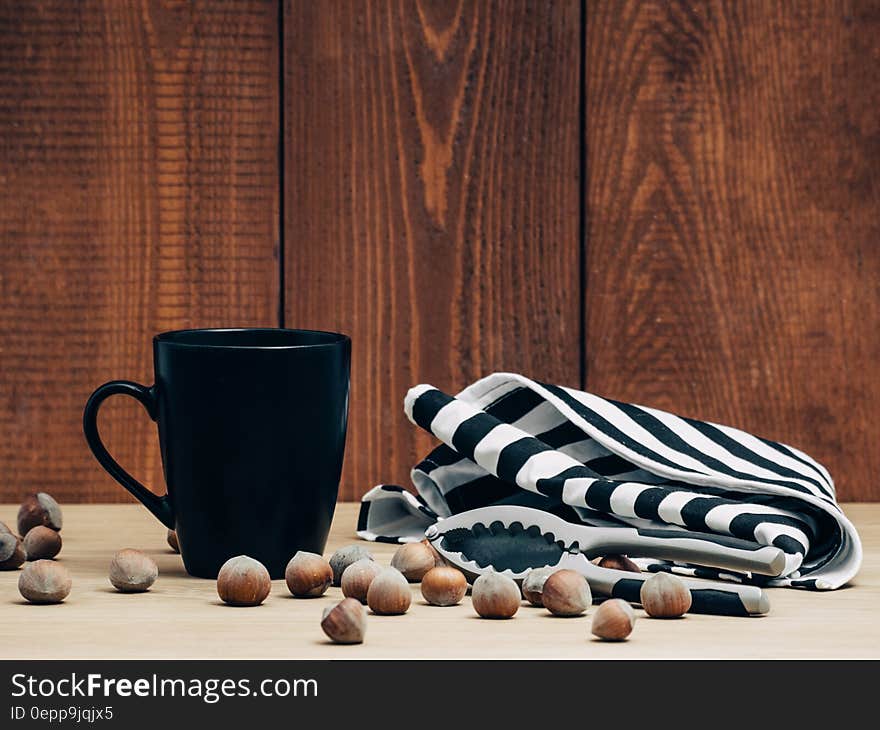 Still life of whole hazelnuts and cracker with black mug and towel against boards. Still life of whole hazelnuts and cracker with black mug and towel against boards.