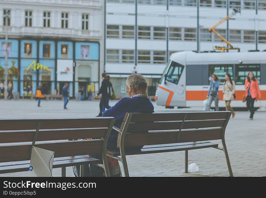 Commuter sitting on city bench next to outdoor tram station. Commuter sitting on city bench next to outdoor tram station.