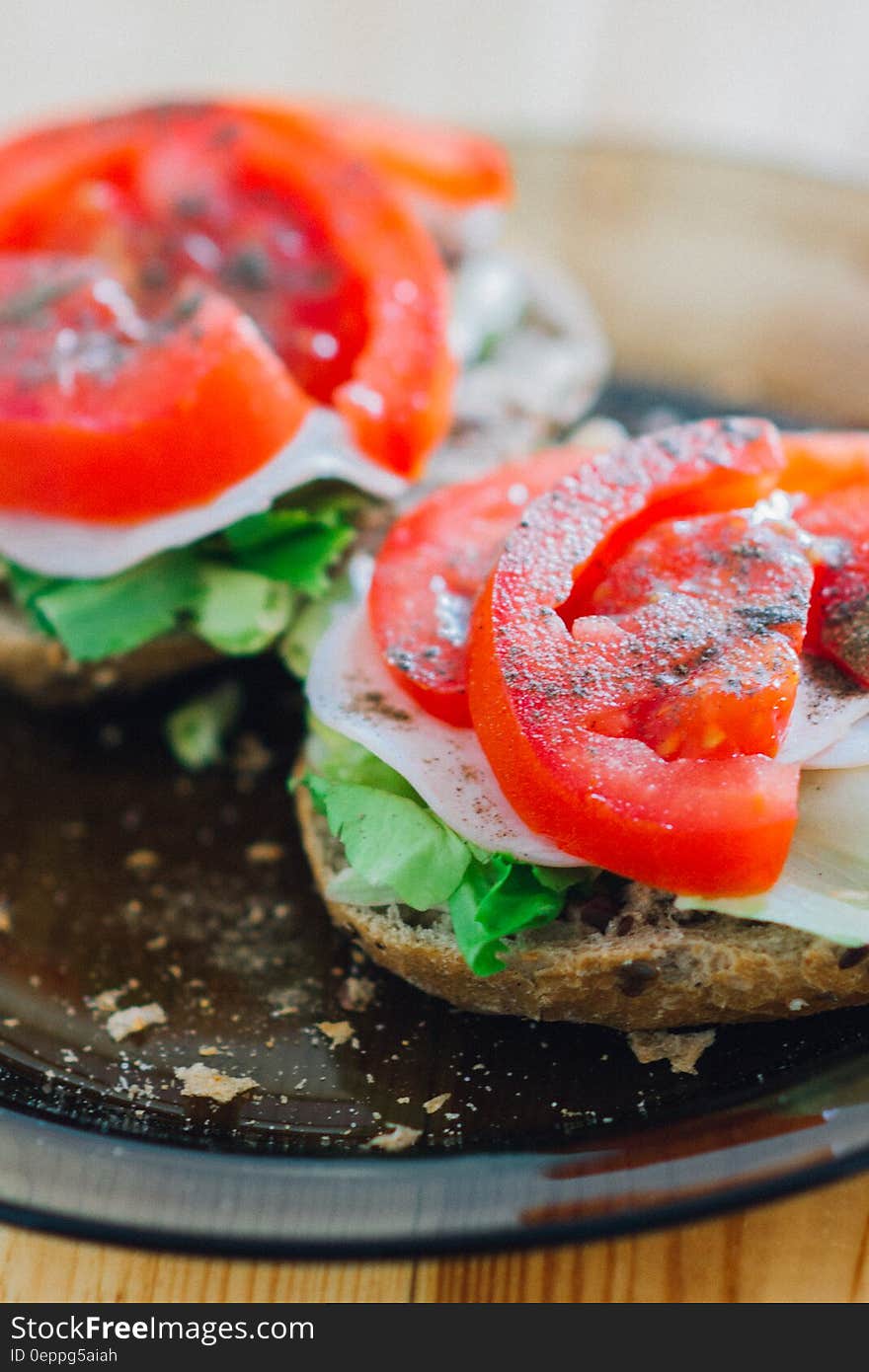 A pair of sandwiches with lettuce and tomato on a plate. A pair of sandwiches with lettuce and tomato on a plate.