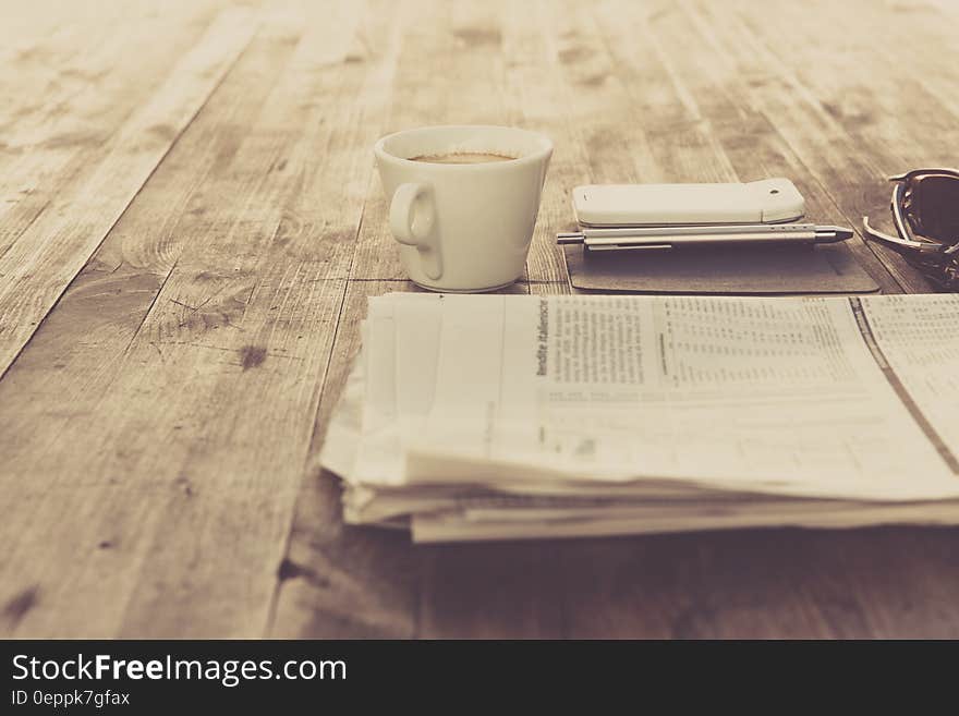 Newspaper and White Ceramic Cup on Brown Wooden Table