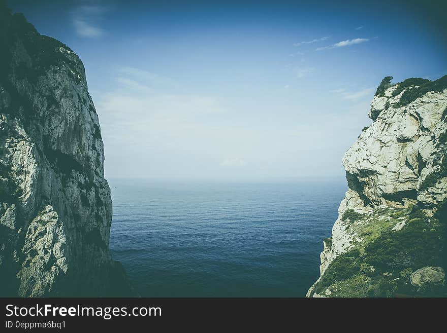 Steep rocky cliffs on coastline with blue sea and cloudscape.