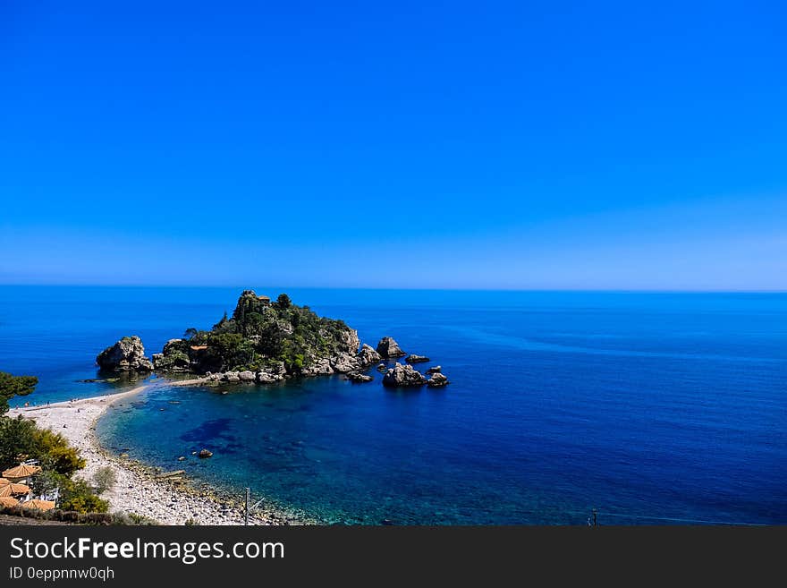 White Beach Shoreline Near Gray Rocks Under Blue Sky during Daytime