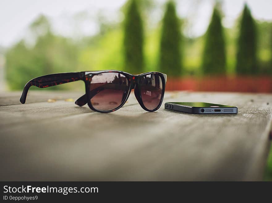 Sunglasses and smartphone outdoors on wooden table.