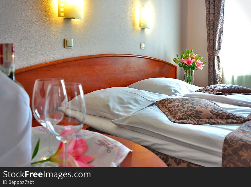 Clear Wine Glass on Brown Wooden Table Top Near Bed