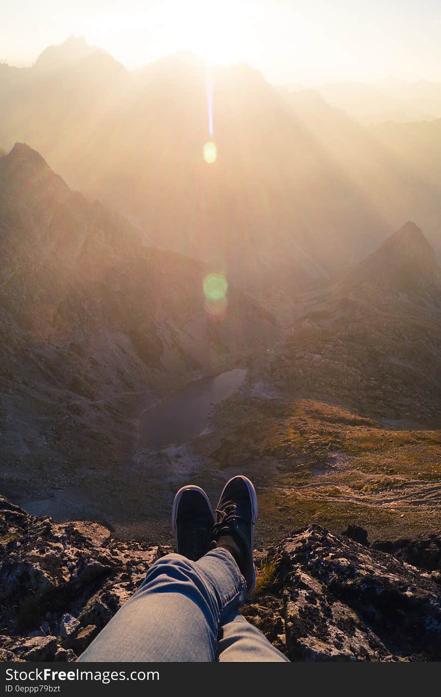 Person Wearing Black Sneakers Sitting in Mountain