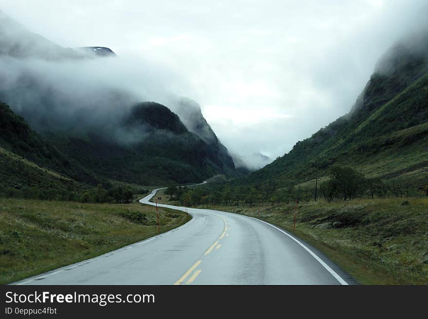 Empty winding roadway through green hillside of mountains in fog. Empty winding roadway through green hillside of mountains in fog.