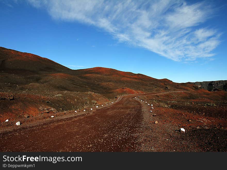 Brown Road Beside Hills over White Clouds and Blue Sky during Daytime