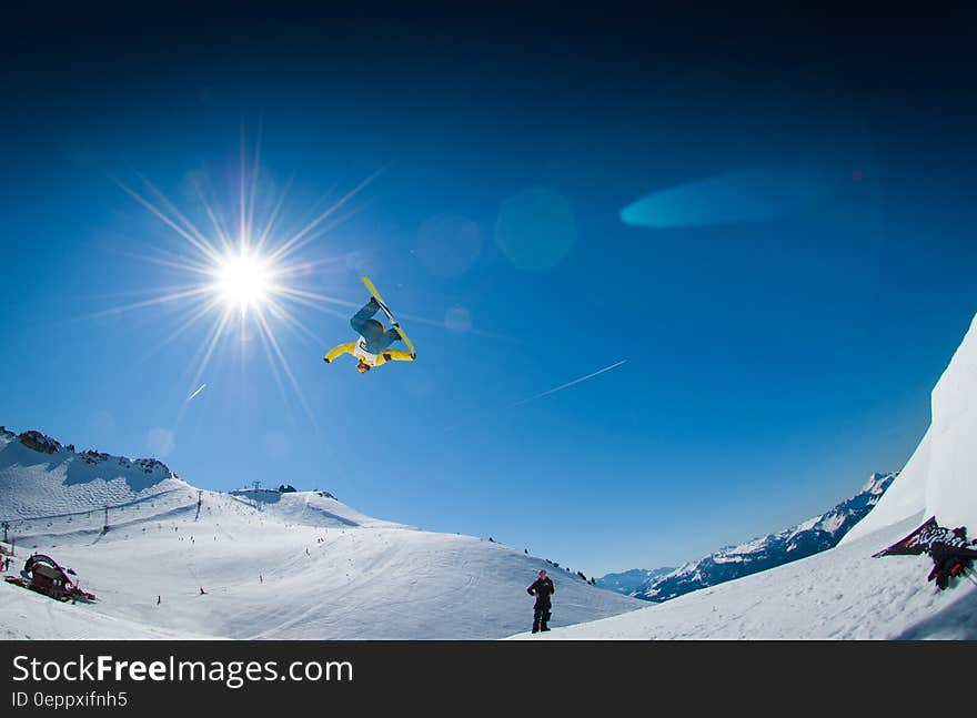 Snowboarder jumping on snowy slopes against blue skies on sunny day.