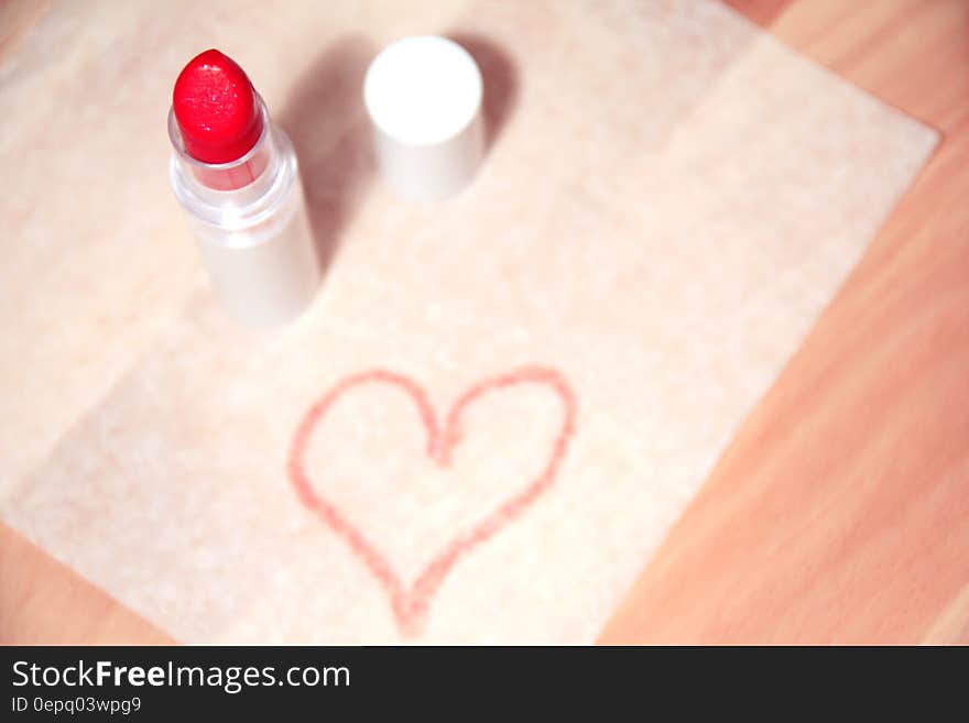 White mat on wooden table with red lipstick uncapped and a red (pink) heart drawn on the mat. Just a hint of love for Saint Valentine's day. White mat on wooden table with red lipstick uncapped and a red (pink) heart drawn on the mat. Just a hint of love for Saint Valentine's day.