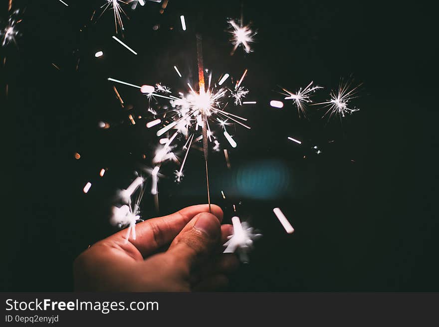 Close up of hand holding lit white sparkler against black. Close up of hand holding lit white sparkler against black.