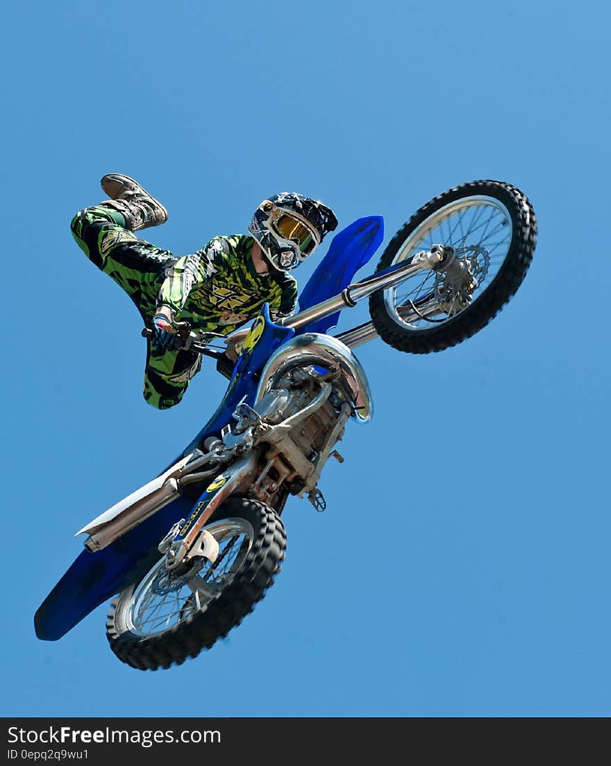 Man riding motocross bike doing acrobatic trick against blue skies on sunny day. Man riding motocross bike doing acrobatic trick against blue skies on sunny day.