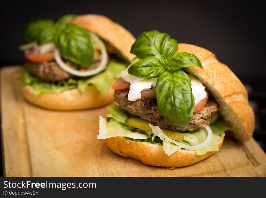 Hamburger sandwiches with lettuce, tomato, onion, pickles, mozzarella cheese and basil on kaiser rolls on wooden cutting board. Hamburger sandwiches with lettuce, tomato, onion, pickles, mozzarella cheese and basil on kaiser rolls on wooden cutting board.