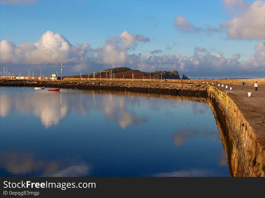 Blue skies and clouds reflecting in blue waters along seawall marina.