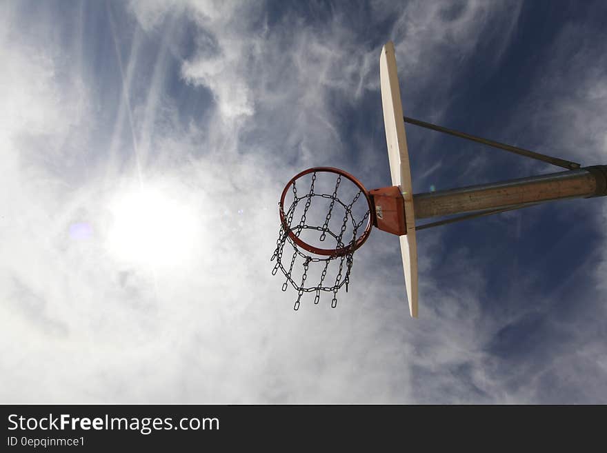 Basketball hoop on rim under backboard against blue skies with clouds on sunny day.