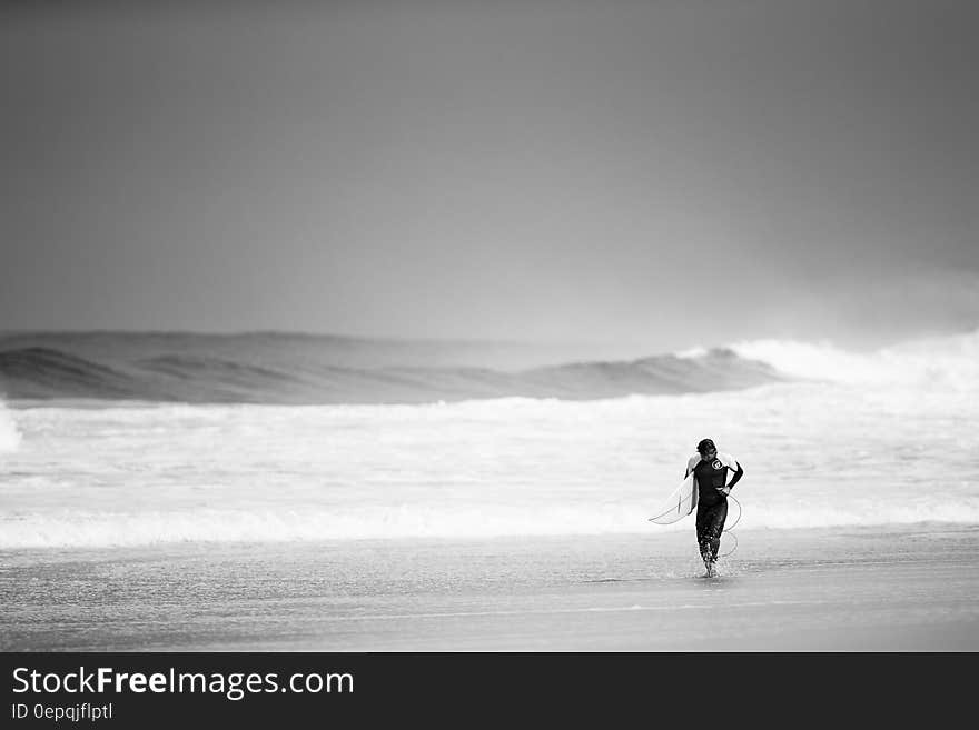 Surfer in wet suit leaving the sea and walking up the beach after surfing on big breaking waves. Surfer in wet suit leaving the sea and walking up the beach after surfing on big breaking waves.