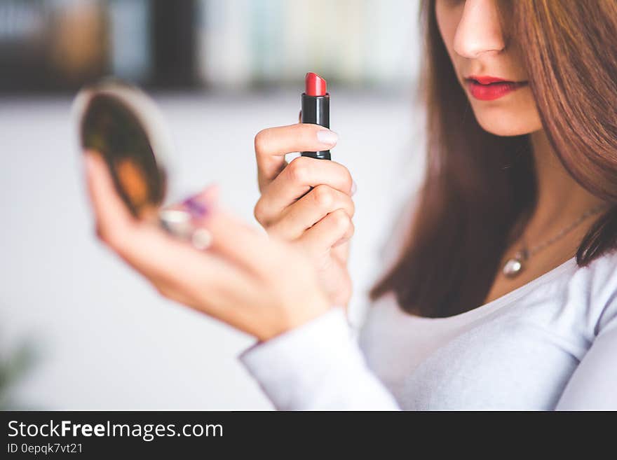 Woman with brown hair doing lipstick and holding little mirror