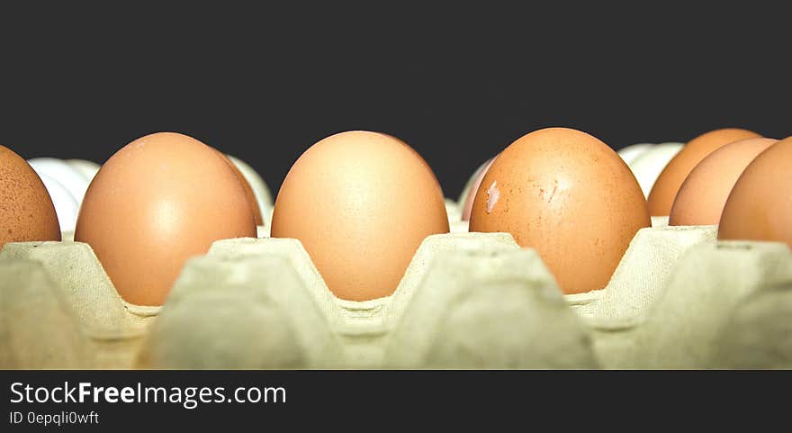 A close up shot of eggs in an egg carton on a black background.