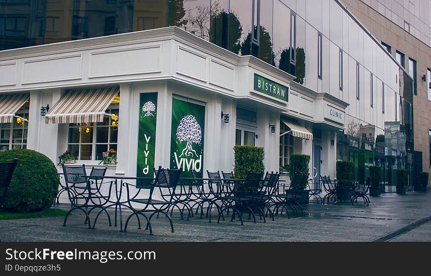 White painted restaurant with the name 'Vivid' in green on the outside walls with tables and chairs on the pavement, seen after closing time and without patrons. White painted restaurant with the name 'Vivid' in green on the outside walls with tables and chairs on the pavement, seen after closing time and without patrons.