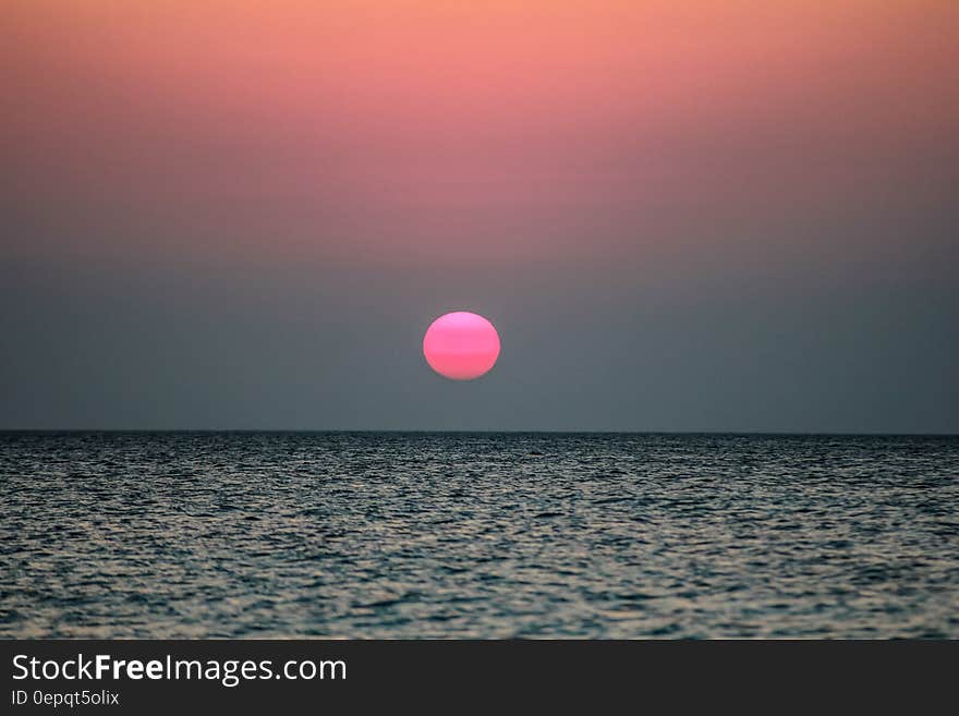 Pink sun setting in skies over ocean waves. Pink sun setting in skies over ocean waves.