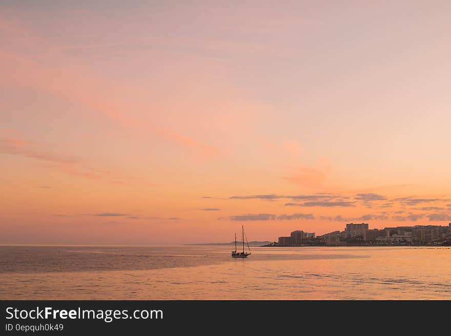 Pink skies at sunset over coastline with sailboat. Pink skies at sunset over coastline with sailboat.