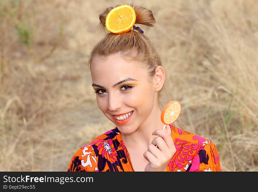 Portrait of woman outdoors in sunny field with orange slice in hair and holding orange lollipop. Portrait of woman outdoors in sunny field with orange slice in hair and holding orange lollipop.