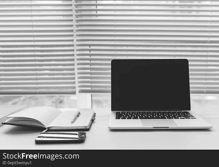 Open laptop computer and notebooks on desktop inside against window with shades in black and white. Open laptop computer and notebooks on desktop inside against window with shades in black and white.