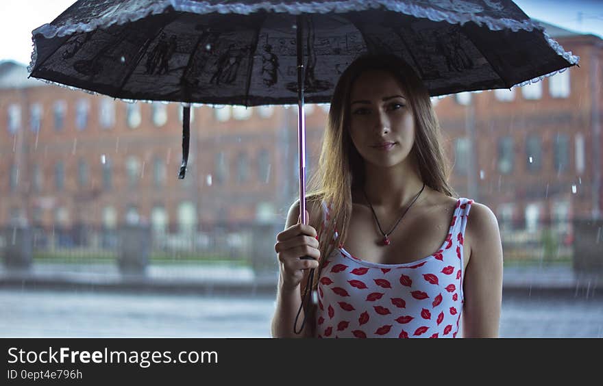 Pretty young woman under an umbrella in the rain with urban buildings in background. Pretty young woman under an umbrella in the rain with urban buildings in background.