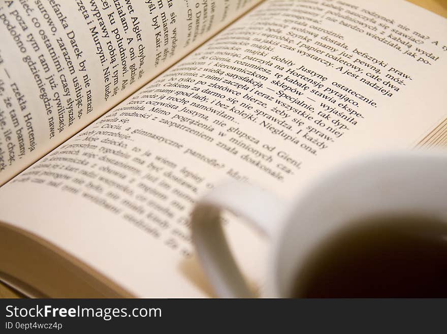 Pages of open book next to white china cup of coffee. Pages of open book next to white china cup of coffee.