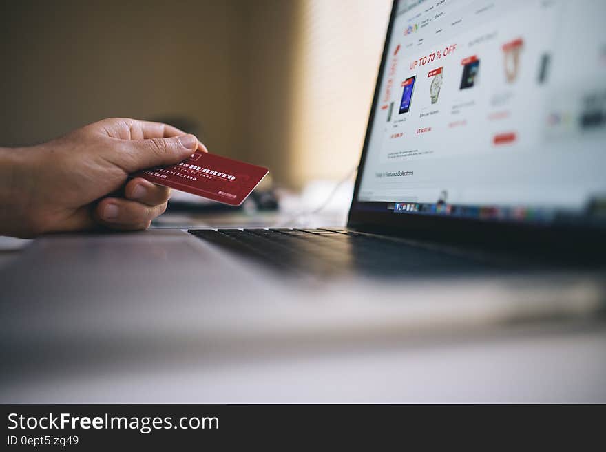 Hand holding credit card next to screen on laptop computer showing sales. Hand holding credit card next to screen on laptop computer showing sales.