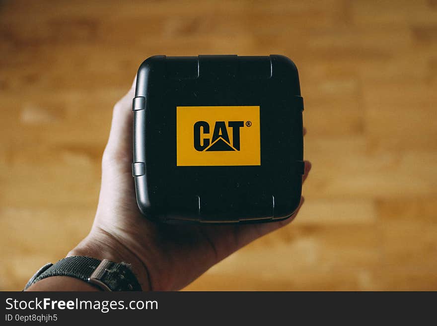 A close up of a hand holding a black box with Caterpillar company logo. A close up of a hand holding a black box with Caterpillar company logo.