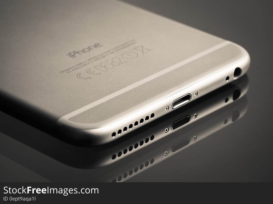 Closeup of iPhone 6 on a dark polished surface showing charger and headphone socket and speaker and reflections.