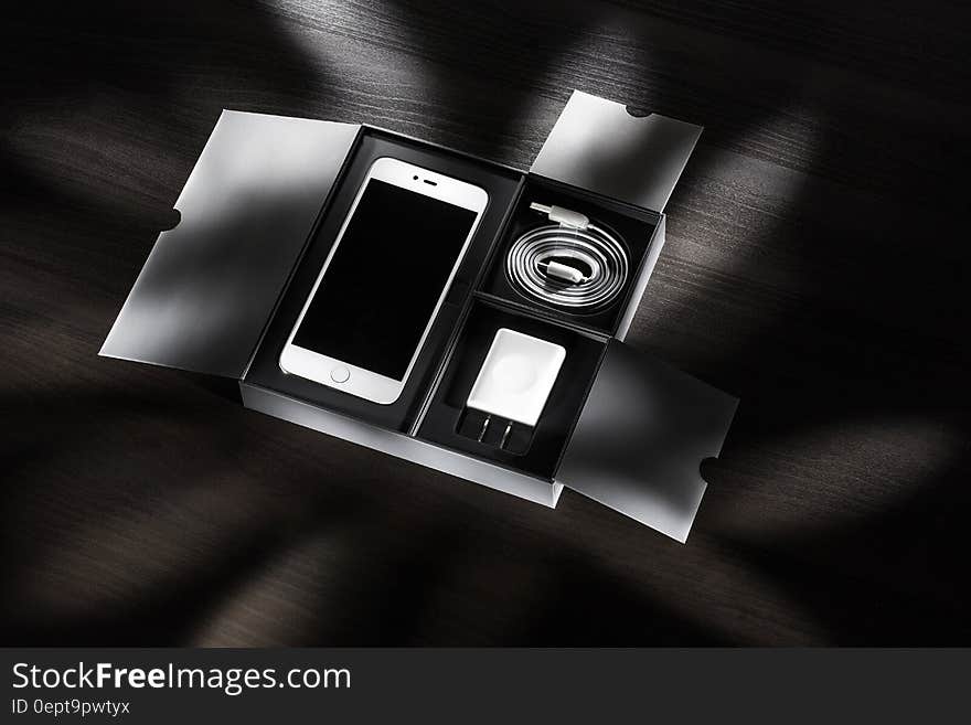 Open box with new smartphone and accessories on desktop in black and white.