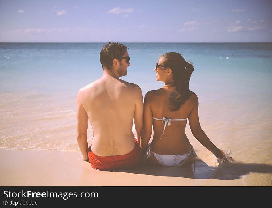 A happy couple sitting on a sandy beach looking at each other. A happy couple sitting on a sandy beach looking at each other.