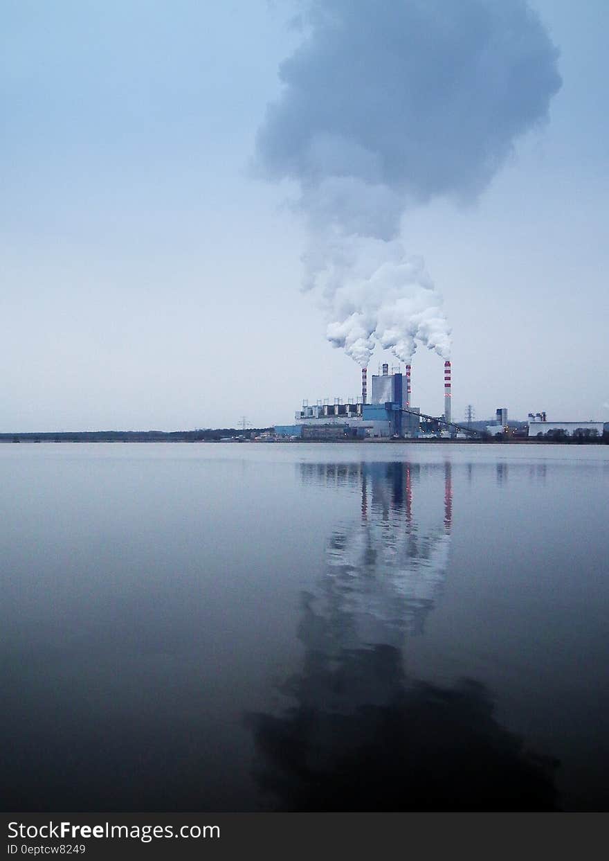 Smoke from factory stacks reflecting in water along shoreline. Smoke from factory stacks reflecting in water along shoreline.