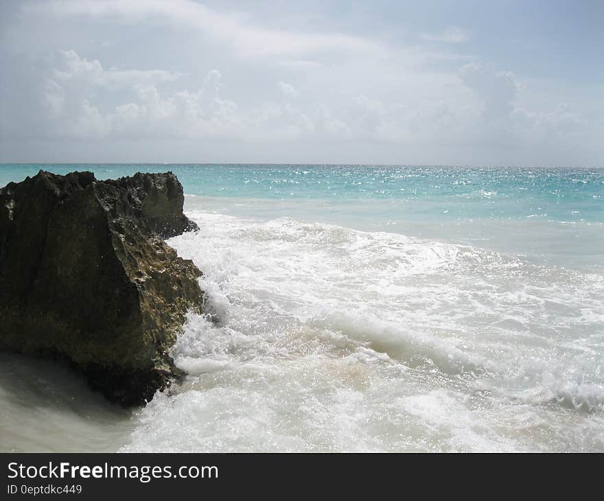 A sharp rock on a sandy beach and the sea splashing against it. A sharp rock on a sandy beach and the sea splashing against it.