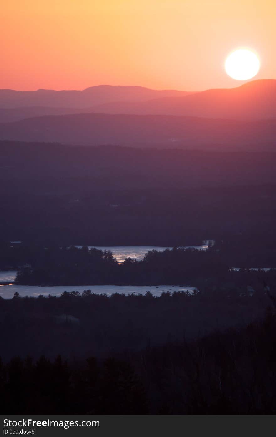 A sunrise seen over the landscape with dark forests, lakes and mountains in the distance. A sunrise seen over the landscape with dark forests, lakes and mountains in the distance.