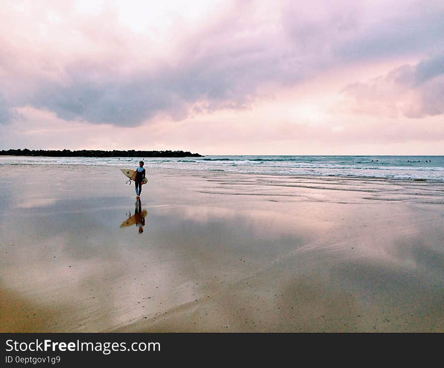 A lonely surfer walking on a sandy beach carrying a surfboard. A lonely surfer walking on a sandy beach carrying a surfboard.