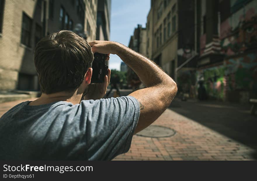 Closeup of young man peering down the cobbled street with shops on the right hand side, blue sky. Closeup of young man peering down the cobbled street with shops on the right hand side, blue sky.