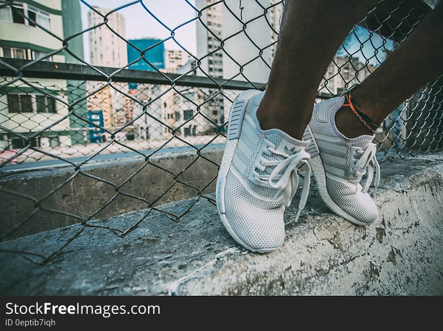 Person Wearing White Adidas Low Top Shoe Near Gray Cyclone Fence