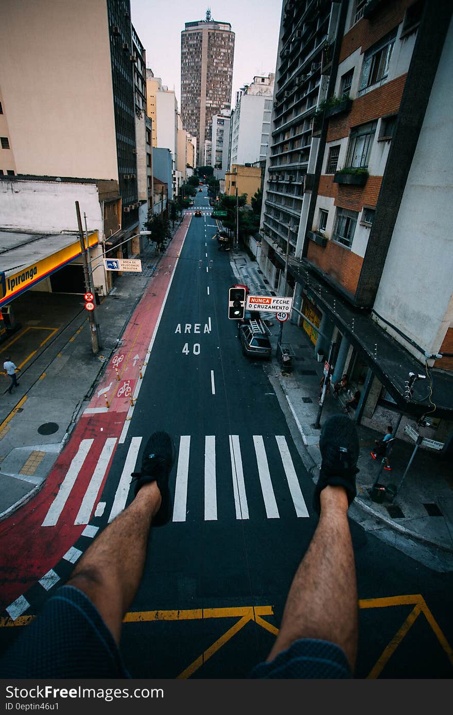 Person Wearing Black Lace Up Sneakers Facing Gray Concrete Road Top Between Concrete Buldings