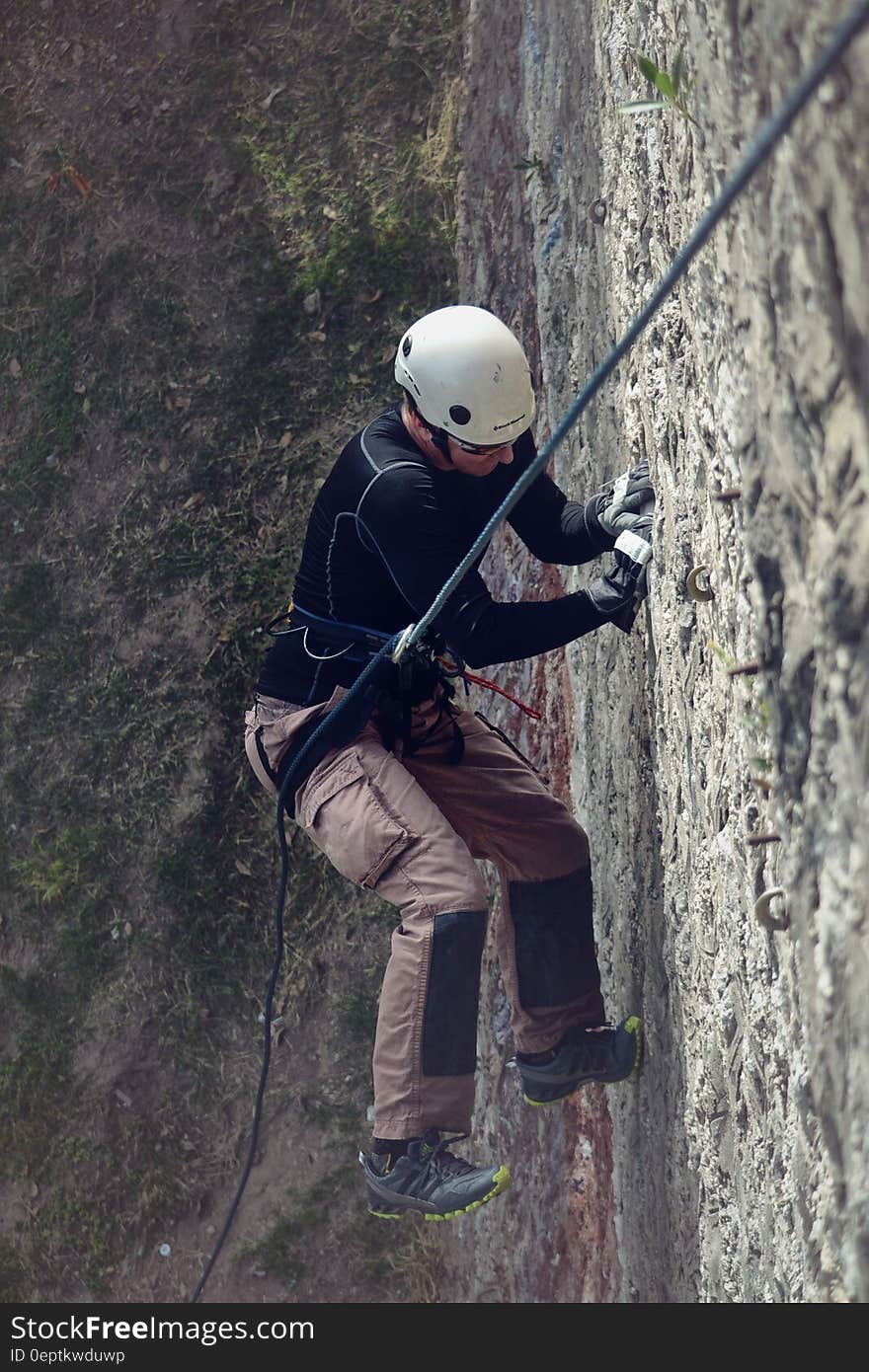 Man in harness using ropes to ascent rock face on sunny day. Man in harness using ropes to ascent rock face on sunny day.