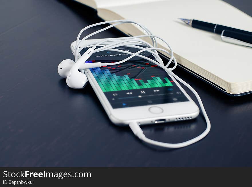 A smartphone with headphones and graph on screen next to a notepad with pen. A smartphone with headphones and graph on screen next to a notepad with pen.