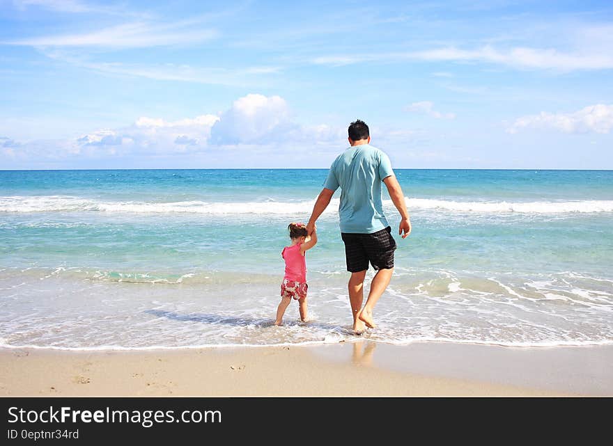 Man and daughter walking in waves on sandy beach on sunny day. Man and daughter walking in waves on sandy beach on sunny day.