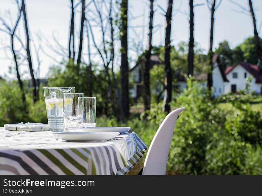 Table and chairs with pitcher of lemonade and glasses in sunny garden. Table and chairs with pitcher of lemonade and glasses in sunny garden.