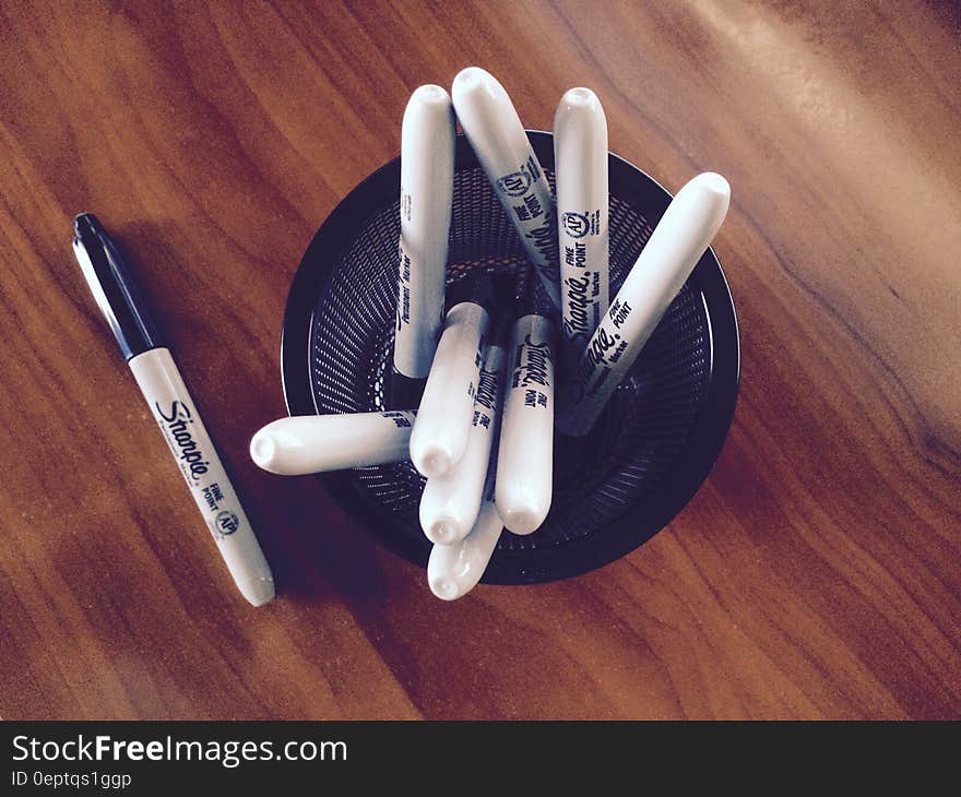 Sharpie black marker pens in cup holder on wooden desk. Sharpie black marker pens in cup holder on wooden desk.