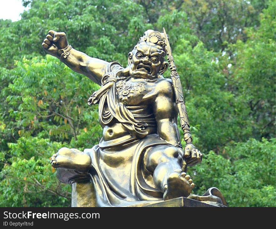 Statue of golden warrior in fight pose outdoors among trees. Statue of golden warrior in fight pose outdoors among trees.