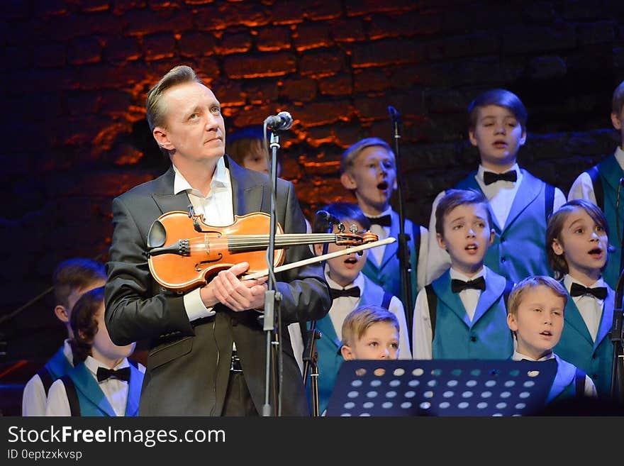 Group of very smart young boys singing with the music master holding a violin beside a microphone and listening to, or judging their rendition or performance. Group of very smart young boys singing with the music master holding a violin beside a microphone and listening to, or judging their rendition or performance.