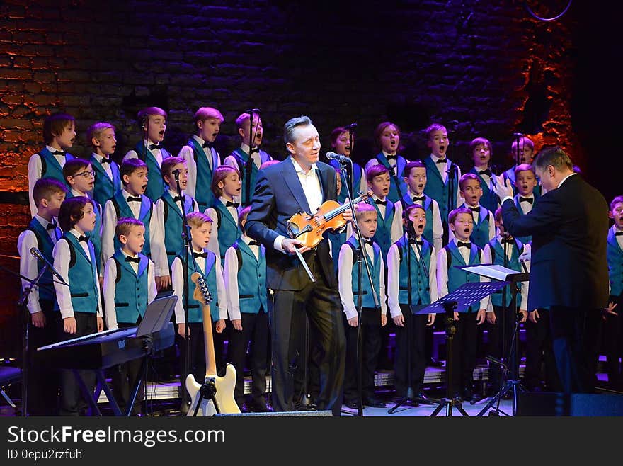 Violinist and children's choir performing onstage with conductor. Violinist and children's choir performing onstage with conductor.