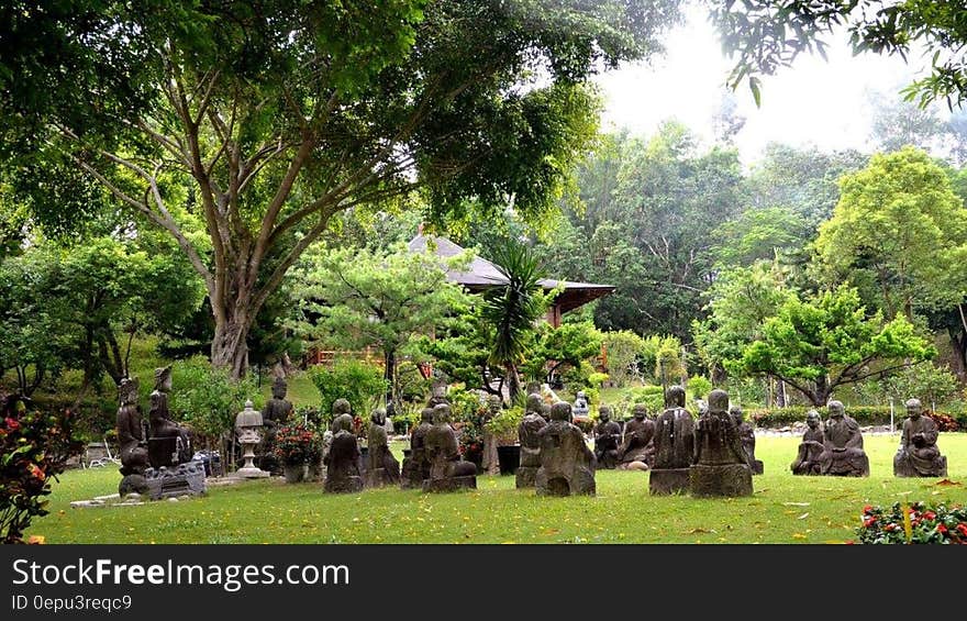 Stone statues in green garden under tree canopy on sunny day. Stone statues in green garden under tree canopy on sunny day.